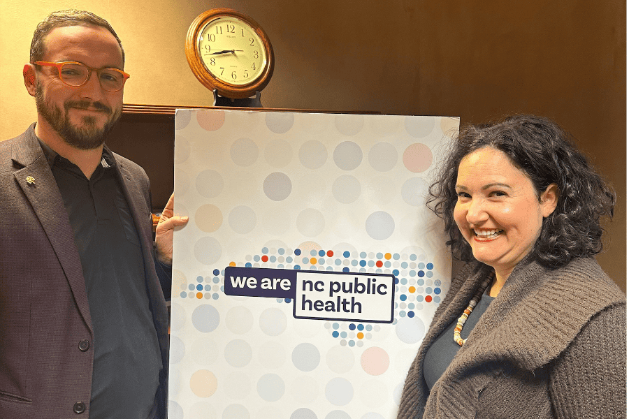 Photo of two North Caroline public health employees holding a sign that says we are nc public health