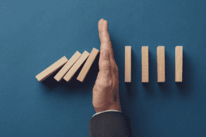 A hand blocking falling tiles from knocking down the other tiles like dominoes.