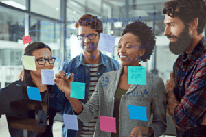 Four coworkers planning and writing on a whiteboard.