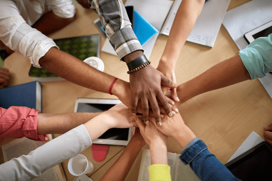 A gathering of people with their hands placed together on a table, representing teamwork and solidarity.