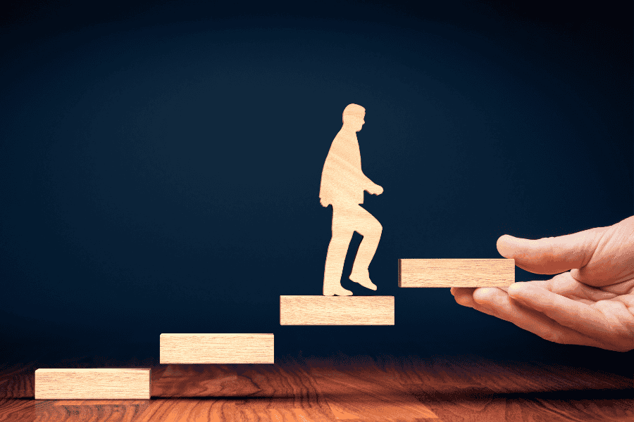 A person holds a wooden figure of a man ascending a staircase, symbolizing progress and movement.