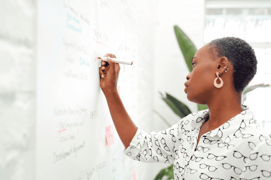 A woman actively writing on a whiteboard, demonstrating engagement in a learning or brainstorming session.
