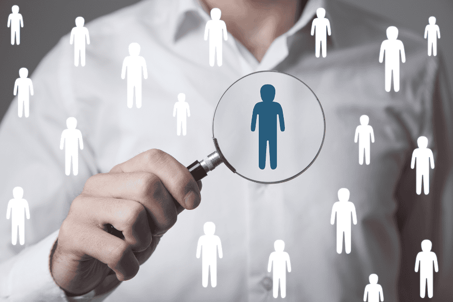 A man examines a group of people closely through a magnifying glass, highlighting attention to detail and observation.