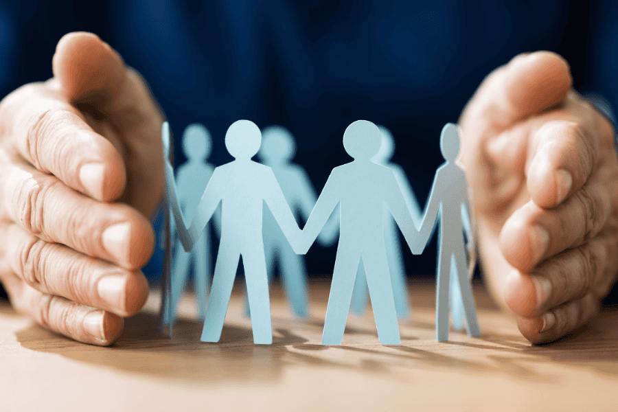 Two hands around a papercut out of people in a circular formation.