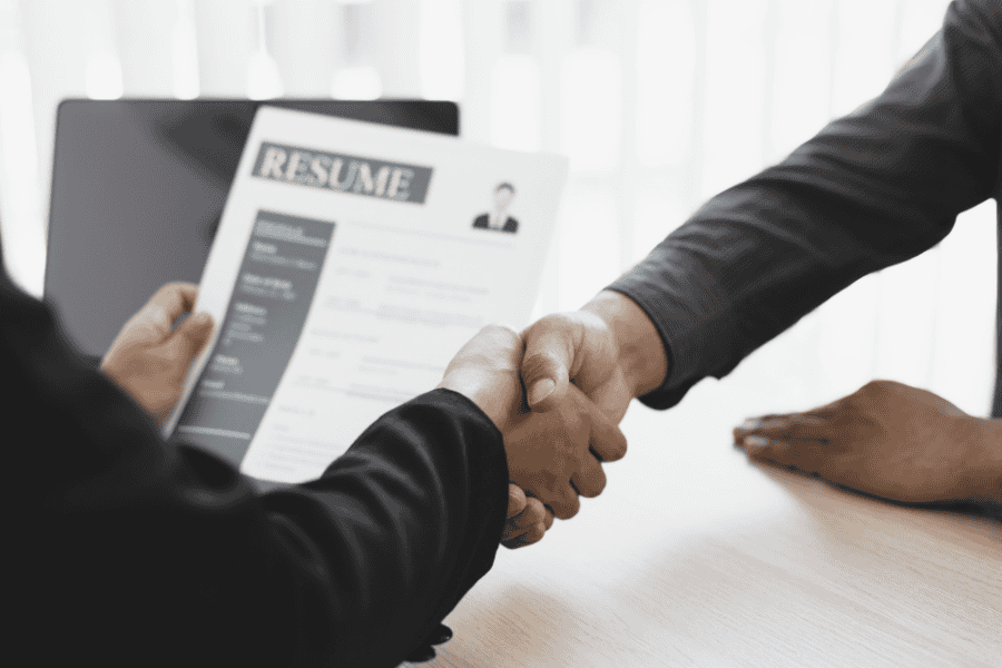 Professionals shaking hands while one person holds a resume.