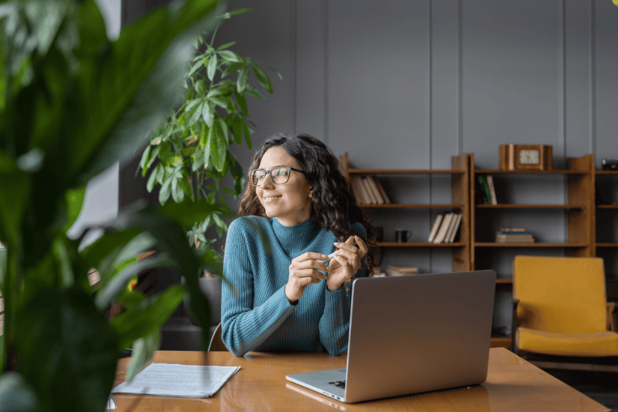 Woman looking off into the distance in front of a laptop.