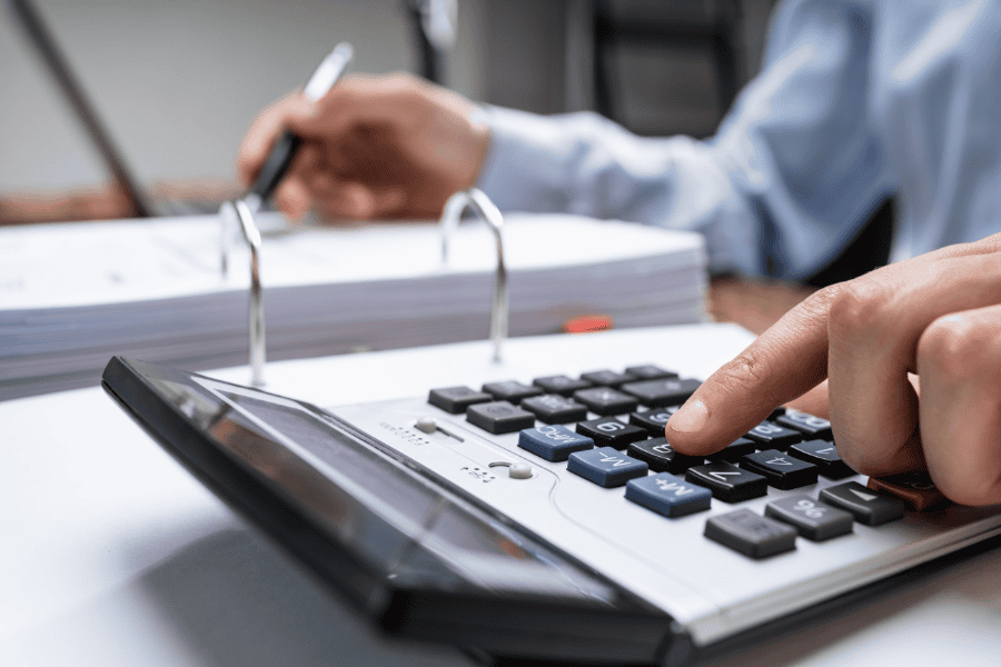 Hands of worker shown using a calculator and taking notes.