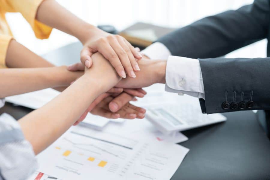 Three people with their hands placed together above a table, representing teamwork and solidarity.