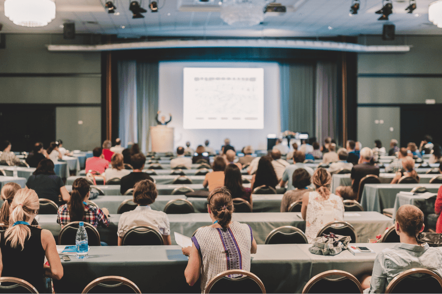 The back of attendee heads as they attend a conference presentation.