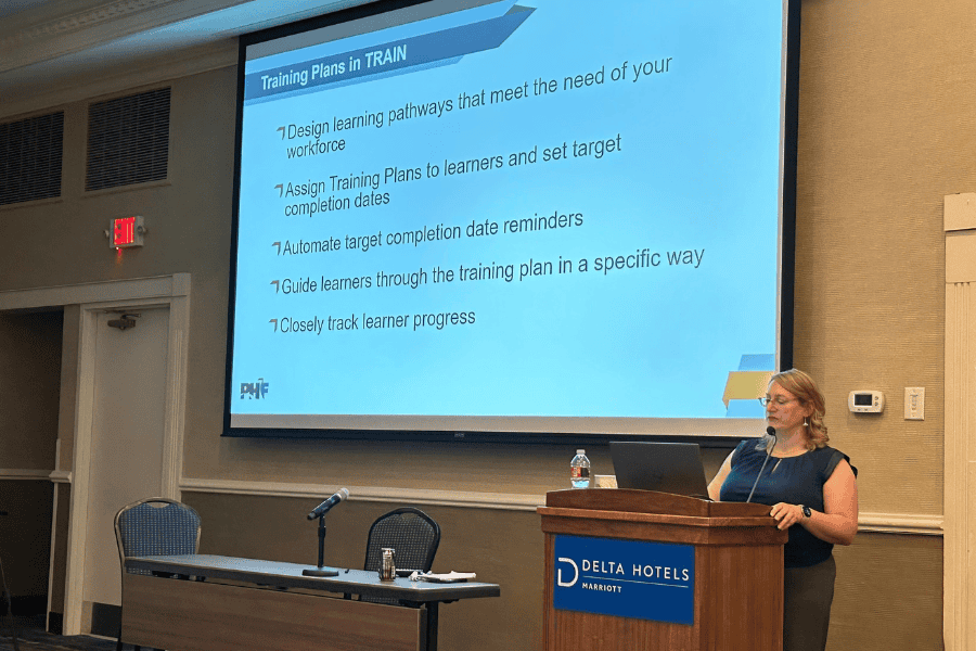 Woman stands at a podium presenting on Montana's virtual training.