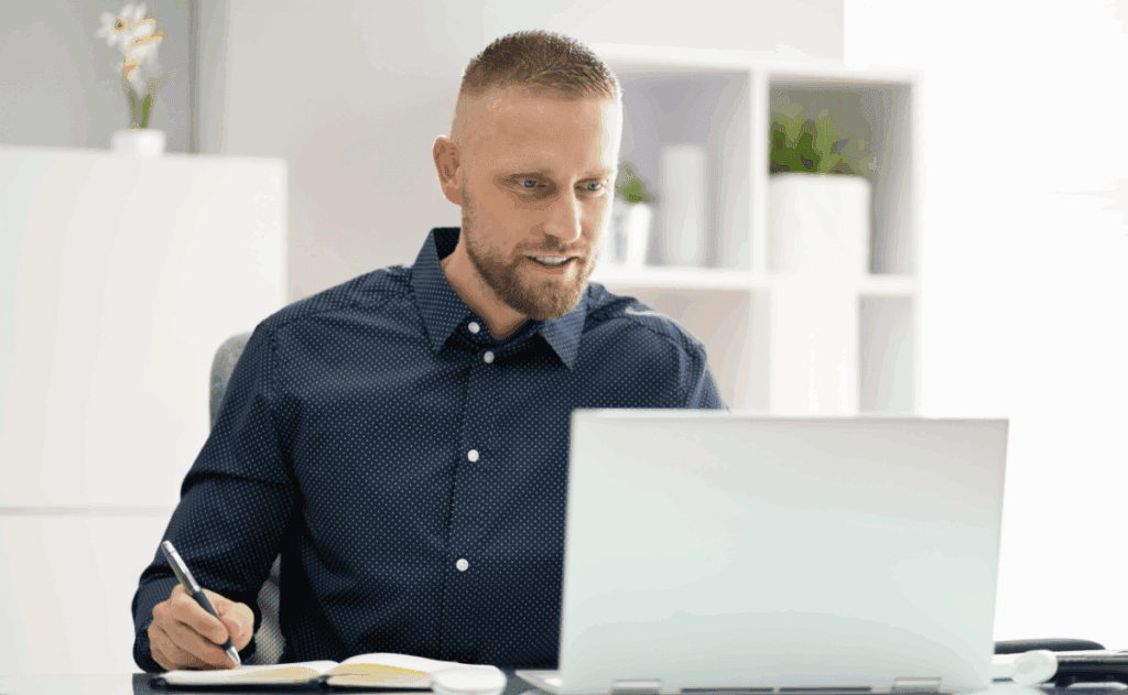 Man takes notes while working at his laptop.