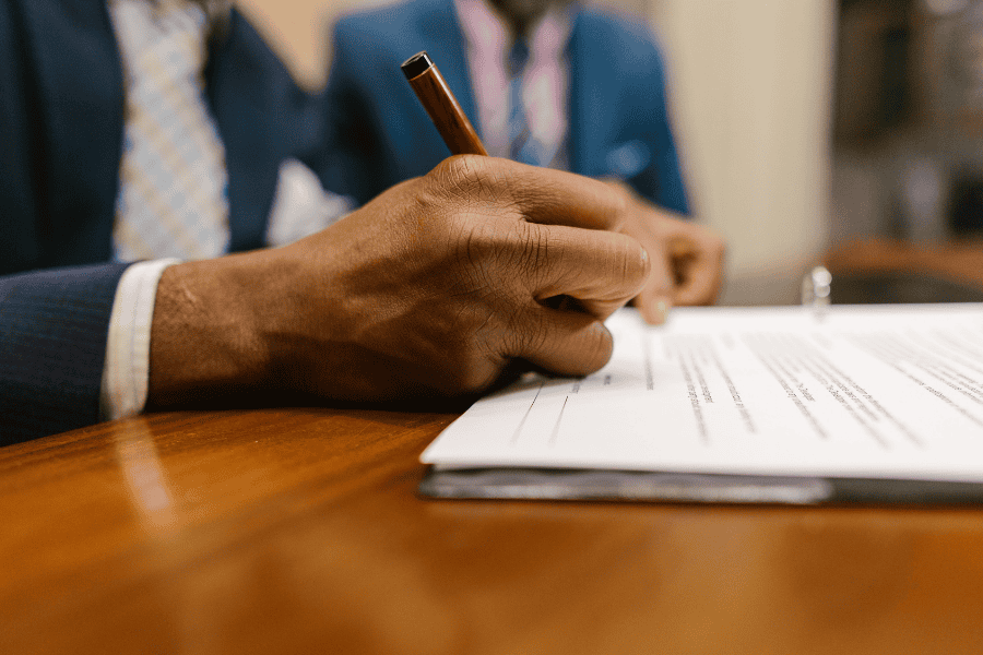 Man's hand signing an official document at a desk.