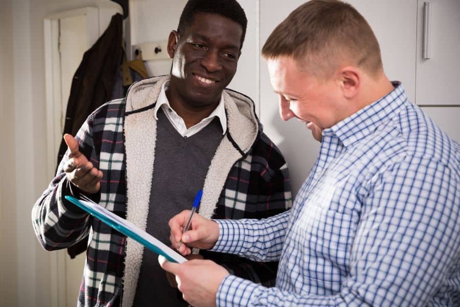A man speaks to another man while holding a clipboard, engaged in a discussion.