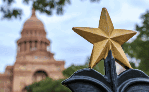 Star in forefront with the Texas Capitol building in the background.