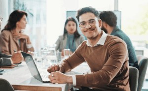 Man in glasses and a business professional outfit sitting at meeting table and smiling directly at the camera.