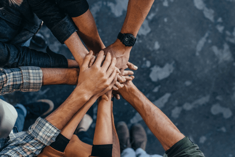 A circle of individuals with their hands placed together, representing teamwork and solidarity among the group.