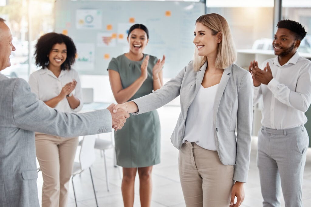 Image of woman shaking hands with someone with team clapping around her.