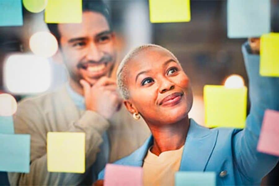 Woman working on planning with post its with her male coworking looking on.