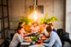 Conceptual image of a team meeting with a lightbulb shining in the foreground.