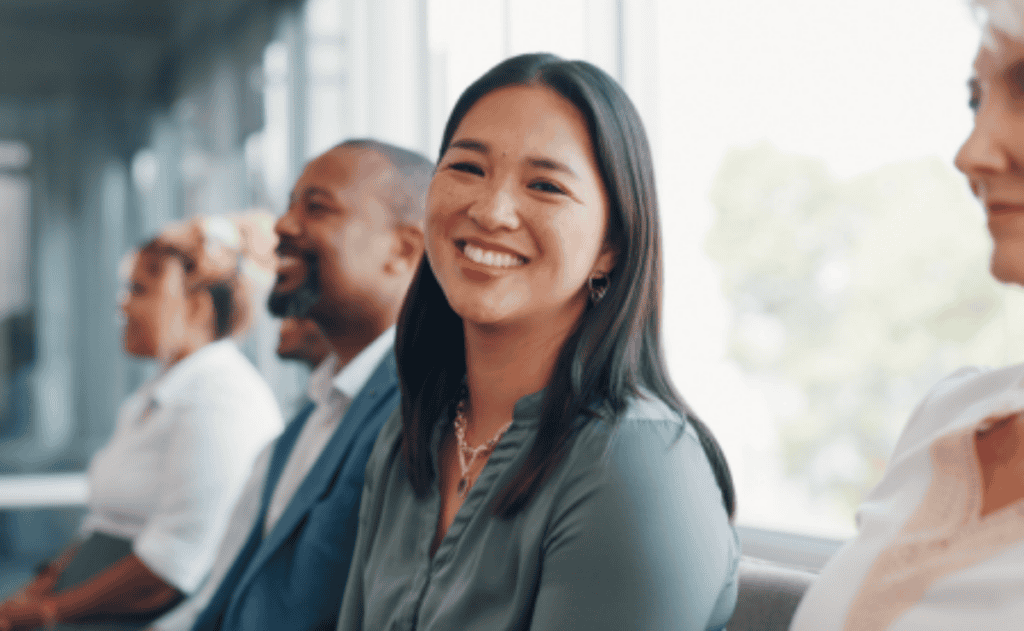 A group of people are sitting in a row, with a woman in the foreground smiling directly at the camera.