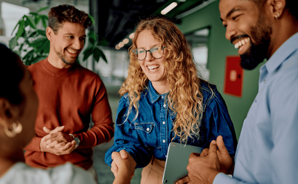 A group of people are smiling and shaking hands in an office setting.