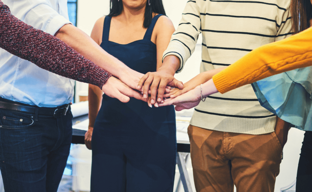 A group of individuals with their hands stacked in a circle, symbolizing teamwork and unity.