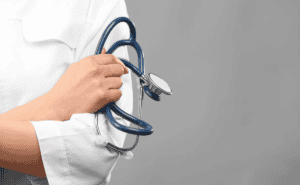 A person in a white coat holds a blue stethoscope across their chest.